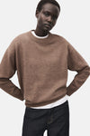 Pull à col rond brun de MANGO, porté sur un t-shirt blanc, avec un jean foncé.