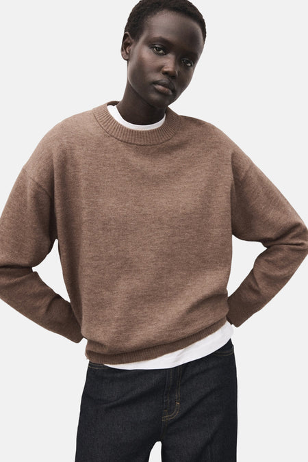Bruine ronde trui van MANGO, gedragen over een wit T-shirt, met een donkere spijkerbroek.