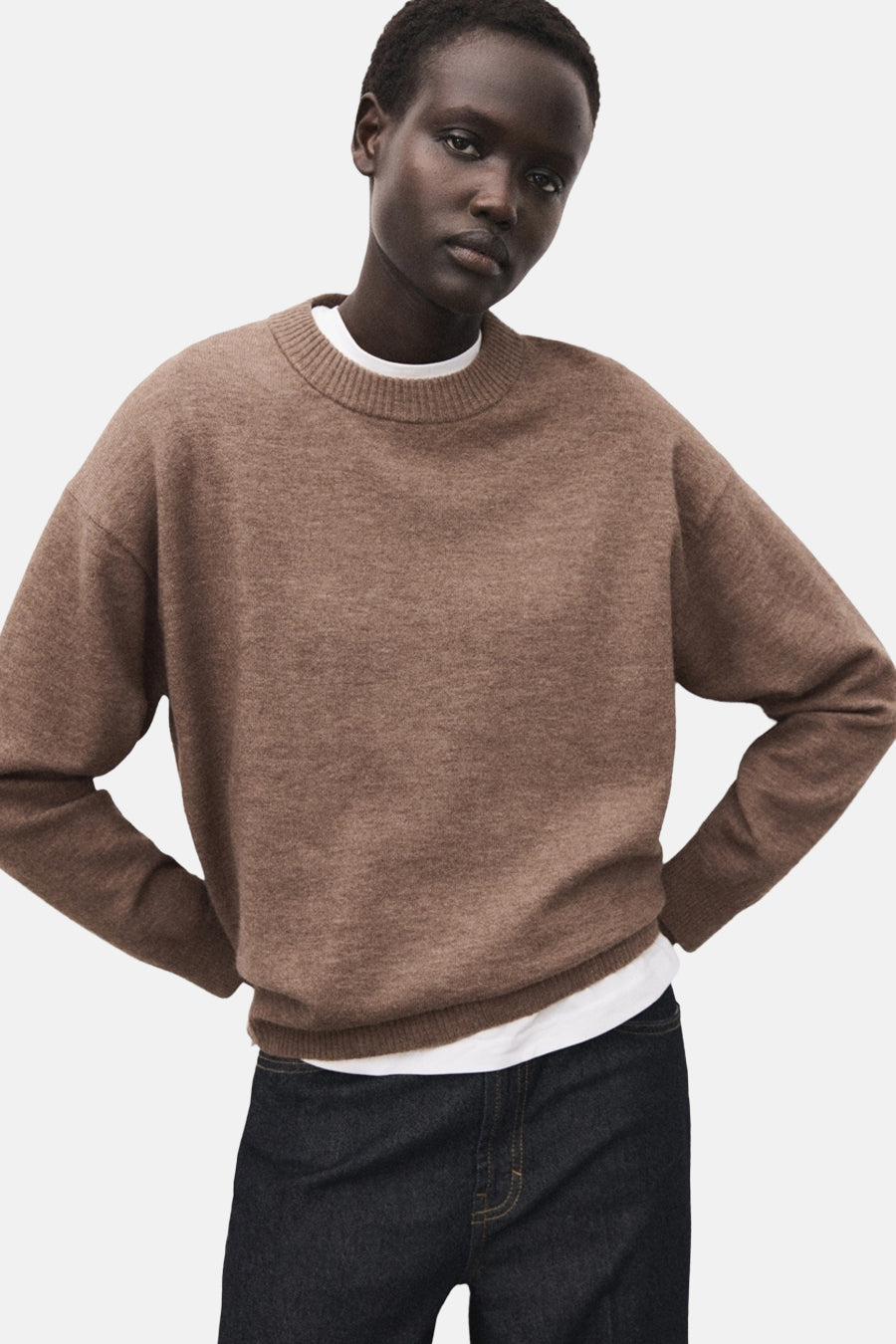 Pull à col rond brun de MANGO, porté sur un t-shirt blanc, avec un jean foncé.