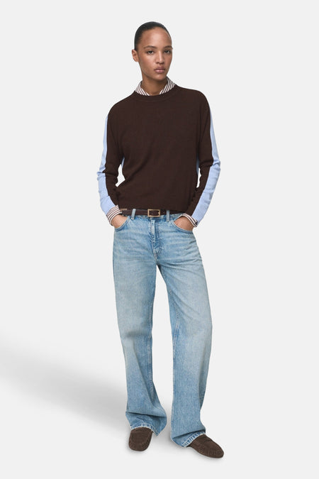 Pull à col rond multicolore de MANGO avec manches longues bleu clair, porté avec un jean ample et une ceinture marron.
