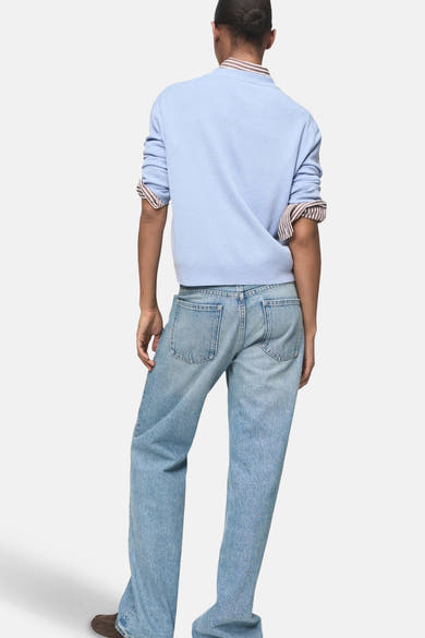 Pull à col rond multicolore de MANGO, manches longues retroussées, porté avec un jean bleu clair décontracté.