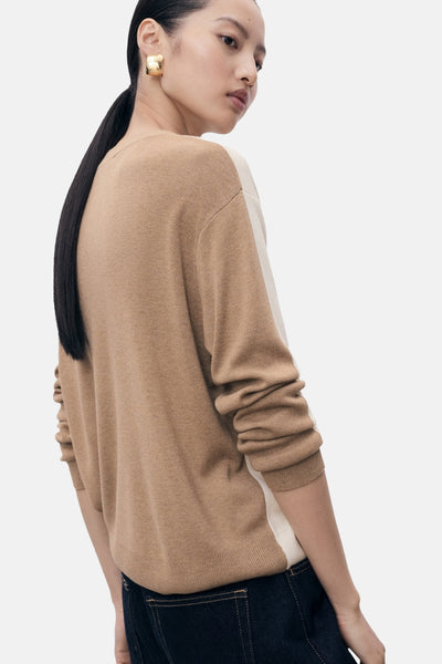 Pull beige à col rond de MANGO, avec bande verticale blanche sur le côté, porté avec un jean bleu foncé.