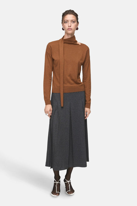 Bruine trui met ronde hals van MANGO, met een asymmetrische kraag en een grijze geplooide rok tot halverwege de kuit.