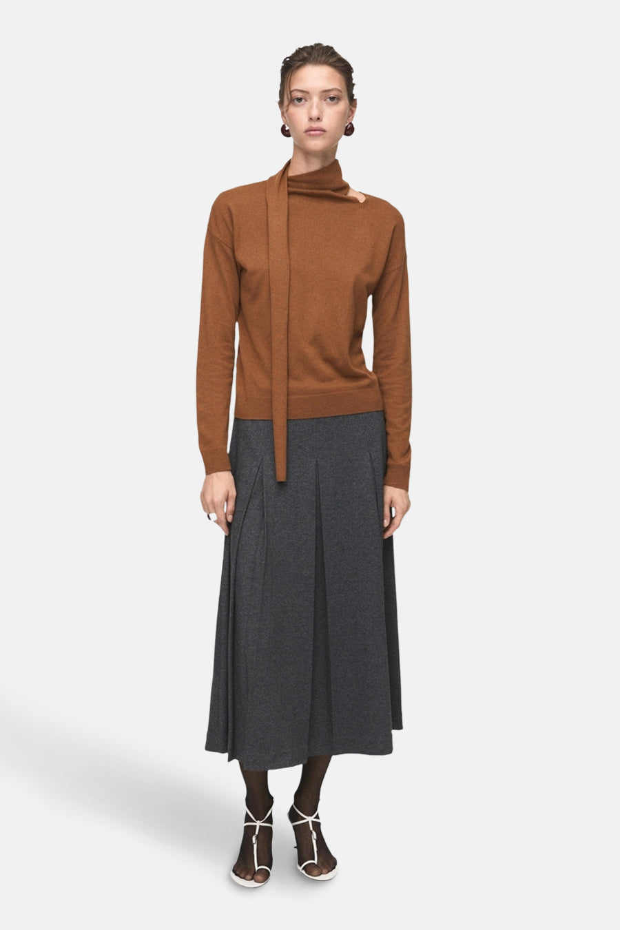 Pull à col rond brun de MANGO, avec un col asymétrique et une jupe plissée grise mi-longueur.