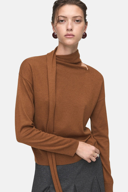 Bruine ronde trui van MANGO met asymmetrische draperiedetails en donkerbruine oorbellen.