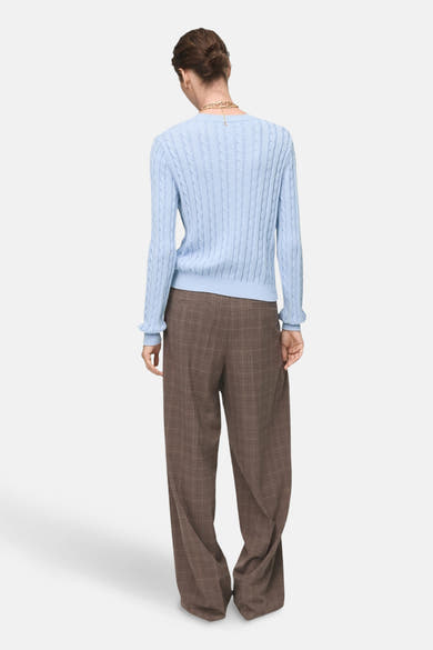 Pull à col rond bleu par MANGO, motif torsadé, porté avec un pantalon à carreaux marron.
