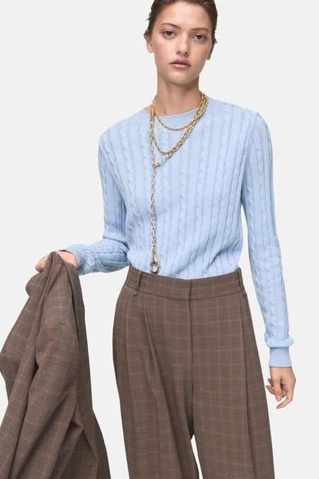 Blauwe trui met ronde hals van MANGO met kabelpatroon, gedragen met een geruite broek en gouden kettingen.