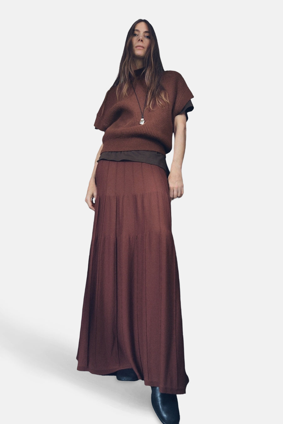 Débardeur brun de MANGO porté avec un collier et une jupe longue plissée, vue en contre-plongée.
