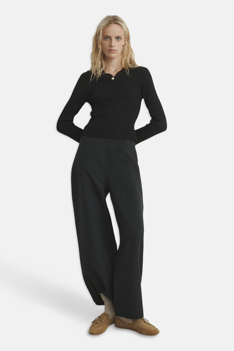 Pull à col rond noir de MANGO, porté avec un pantalon ample gris foncé et des chaussures en daim marron.