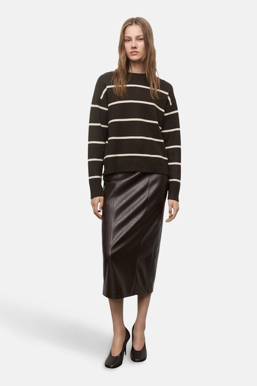 Pull à col rond marron par MANGO, rayures horizontales blanches, porté avec une jupe en cuir marron et des escarpins noirs.