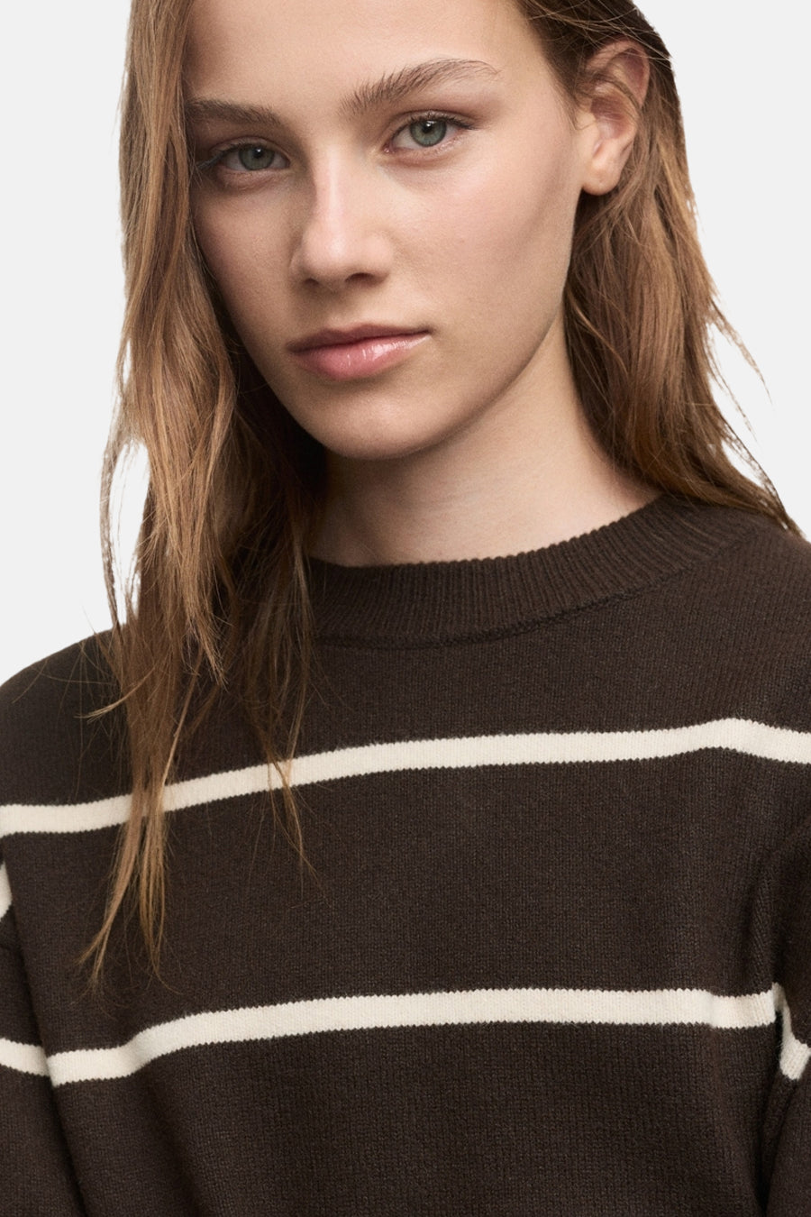 Bruine ronde trui van MANGO, met witte horizontale strepen, gedragen door een model met lang haar.