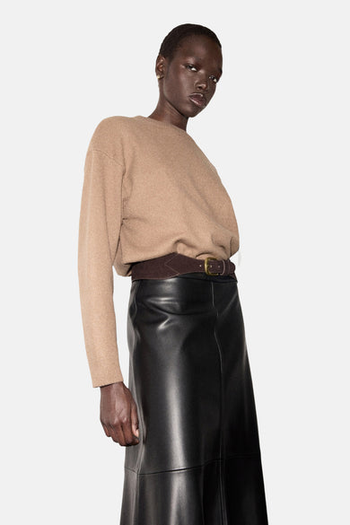 Pull à col rond marron by MANGO, porté avec une jupe noire en similicuir et une ceinture marron.