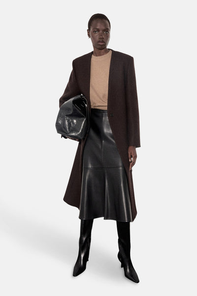 Pull à col rond brun de MANGO, porté avec une jupe noire en cuir et des bottes assorties.
