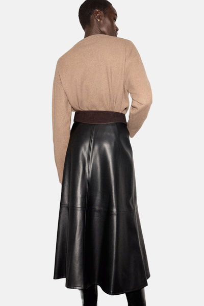 Pull à col rond marron de MANGO, porté avec une jupe noire en similicuir et une ceinture marron.