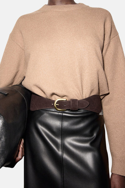 Pull à col rond brun de MANGO, porté avec une ceinture marron en daim et une jupe noire en cuir.