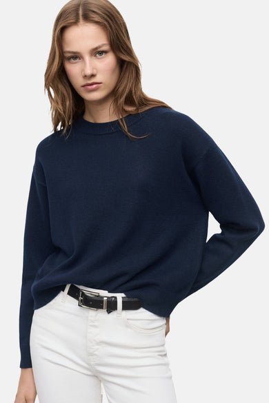 Pull à col rond bleu de MANGO porté avec un jean blanc et une ceinture noire.
