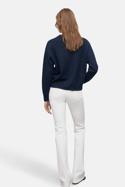 Pull à col rond bleu de MANGO, porté avec un jean blanc évasé, vue de dos.