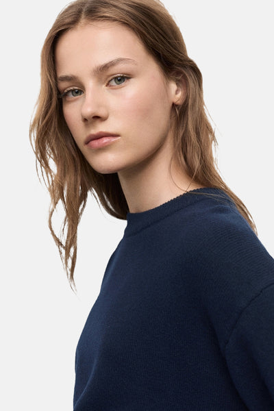 Pull bleu à col rond de MANGO, en maille fine, porté par une femme regardant vers la caméra.