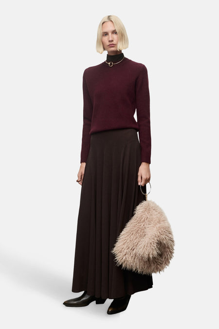 Pull à col rond bordeaux de MANGO, porté avec une jupe longue évasée et un collier doré ras du cou.