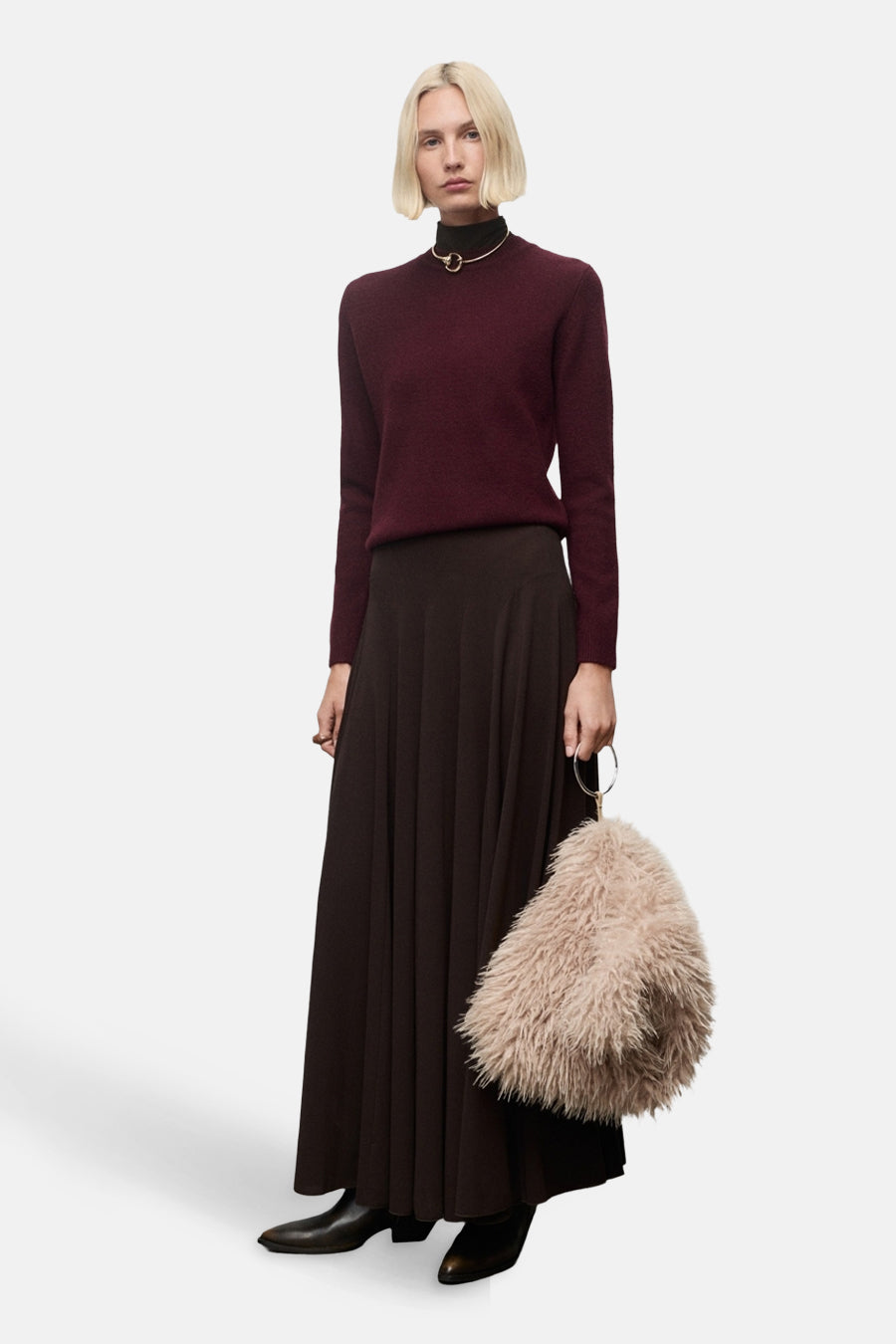 Pull à col rond bordeaux de MANGO, porté avec une jupe longue évasée et un collier doré ras du cou.