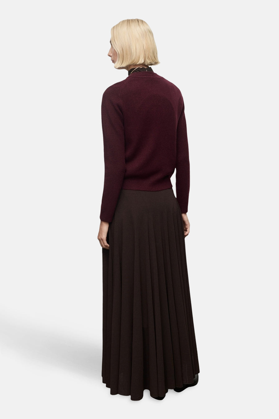 Pull à col rond bordeaux de MANGO, porté avec une jupe longue plissée marron, vue de dos.
