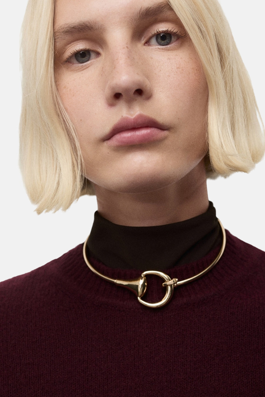 Pull à col rond bordeaux de MANGO, porté avec un collier doré original et un col roulé marron.