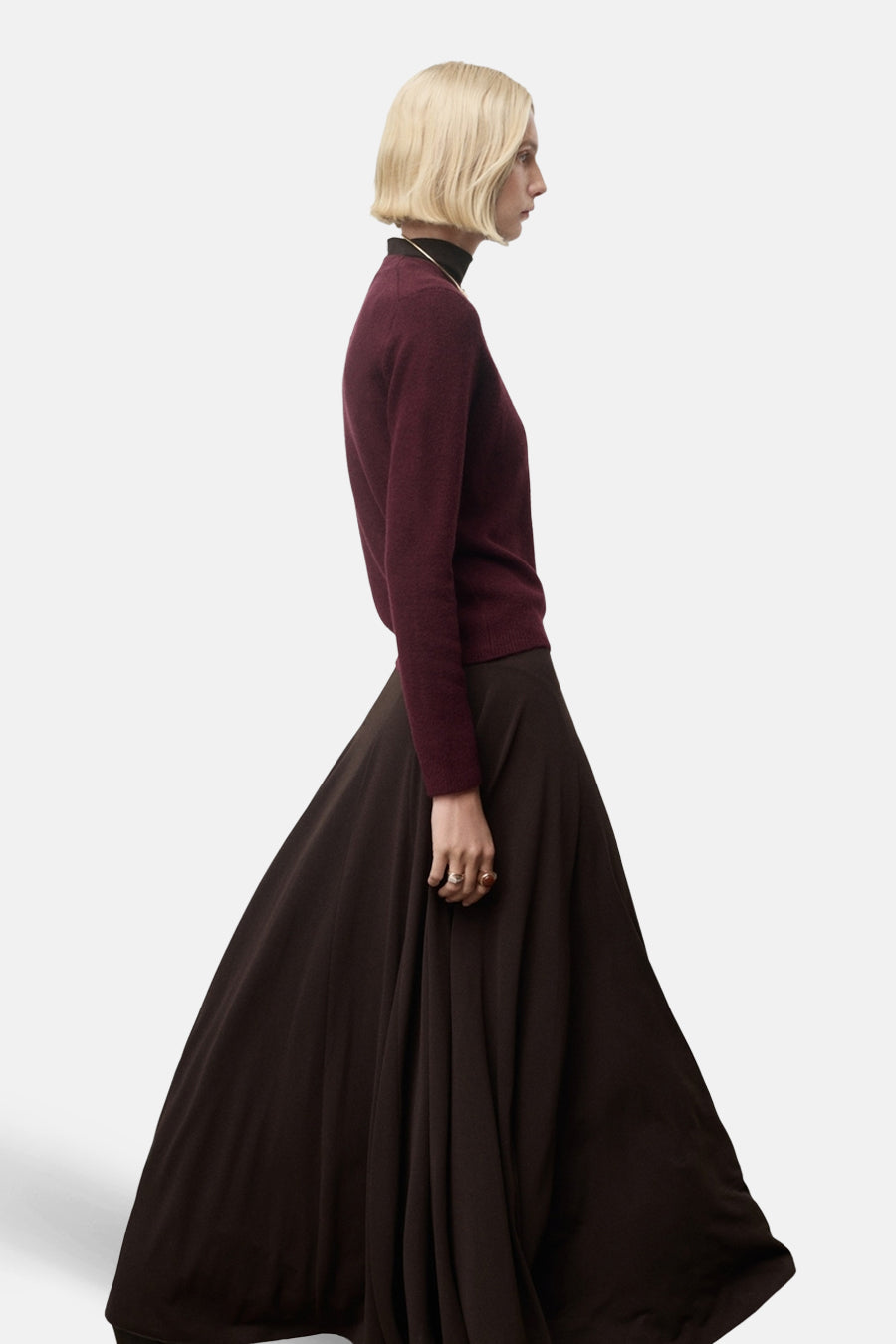 Pull à col rond bordeaux de MANGO, porté avec un col roulé noir et une longue jupe marron.
