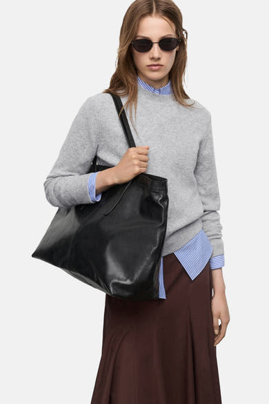 Pull à col rond gris de MANGO, porté avec une chemise rayée bleue et une jupe marron.