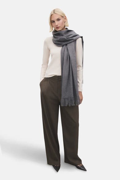 Pull à col rond écru de MANGO, porté avec un pantalon large marron et une écharpe grise à franges.