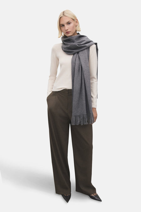 Pull à col rond écru de MANGO, porté avec un pantalon large marron et une écharpe grise à franges.