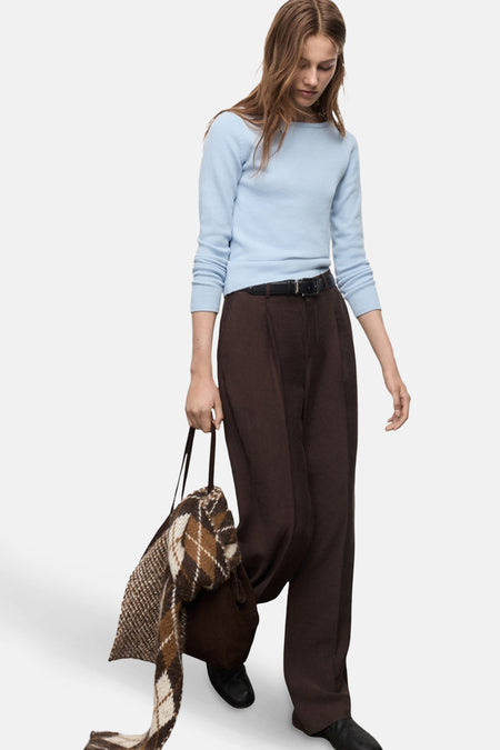 Pull à col rond bleu de MANGO, porté avec un pantalon marron taille haute et un sac en daim marron à motif losanges.
