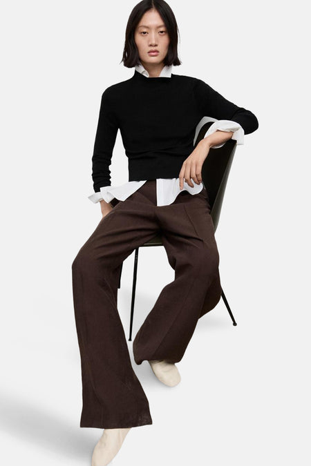 Pull à col rond noir de MANGO, porté avec une chemise blanche et un pantalon marron ample.