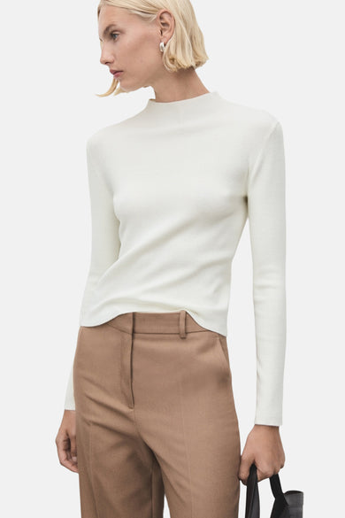 Pull à col rond écru de MANGO, porté avec un pantalon marron taille haute et un sac noir.