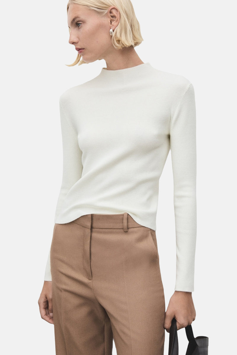 Pull à col rond écru de MANGO, porté avec un pantalon marron taille haute et un sac noir.
