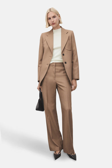 Pull à col rond écru de MANGO, porté sous un blazer et un pantalon marron, avec des escarpins noirs.
