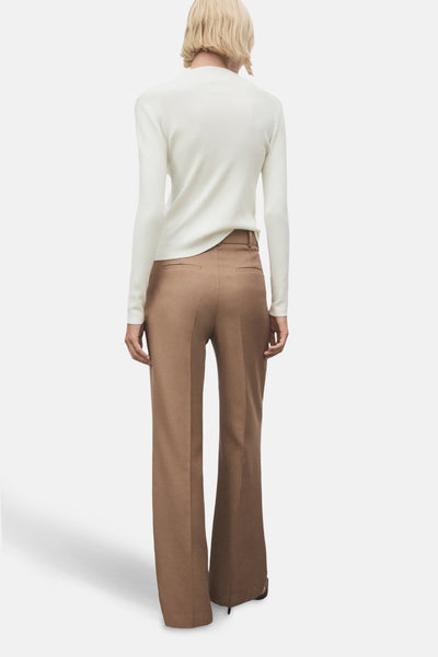 Pull à col rond écru de MANGO, porté avec un pantalon marron taille haute et jambes évasées.