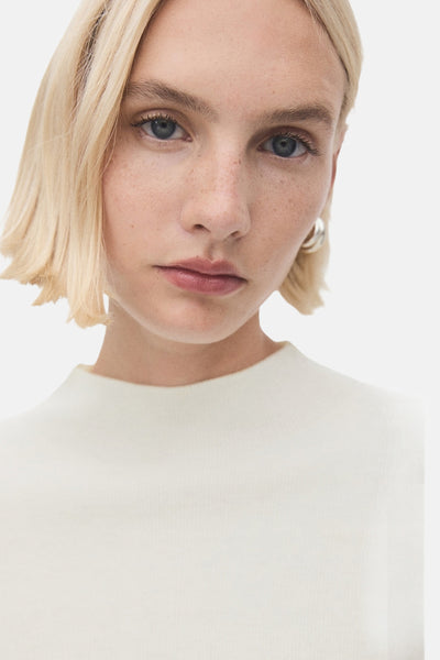 Pull écru à col rond de MANGO, porté avec des boucles d'oreilles argentées, en gros plan.