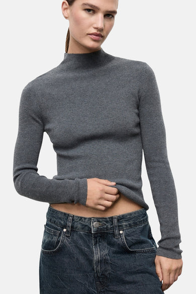 Pull à col rond gris de MANGO, en maille côtelée, porté avec un jean taille basse.
