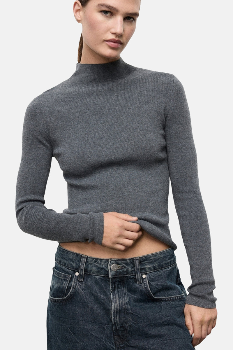 Pull à col rond gris de MANGO, en maille côtelée, porté avec un jean taille basse.
