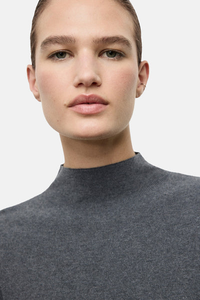 Pull à col rond gris de MANGO en tricot côtelé fin, porté avec un petit anneau à l'oreille.
