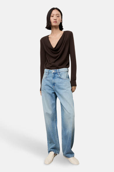 Pull à col rond brun de MANGO, porté avec un jean bleu ample et des chaussures beiges.
