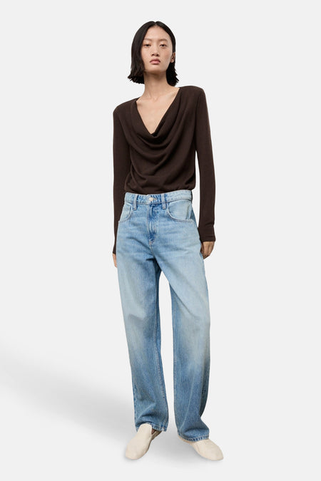 Pull à col rond brun de MANGO, porté avec un jean bleu ample et des chaussures beiges.
