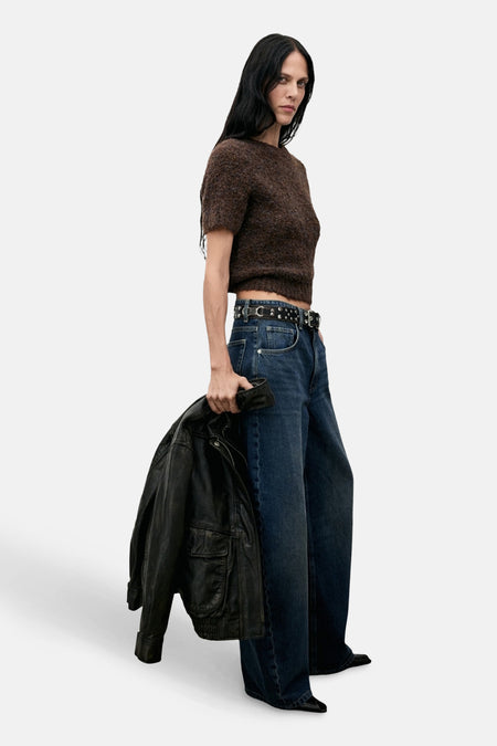 Pull à col rond brun de MANGO, porté avec un jean taille haute, une ceinture cloutée et un blouson en cuir.