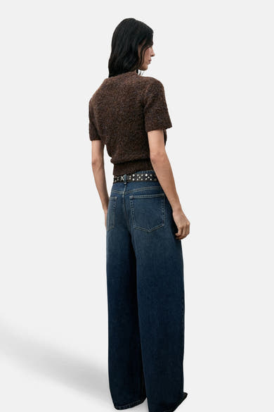 Pull à col rond brun de MANGO, porté avec une ceinture cloutée et un jean large bleu foncé.