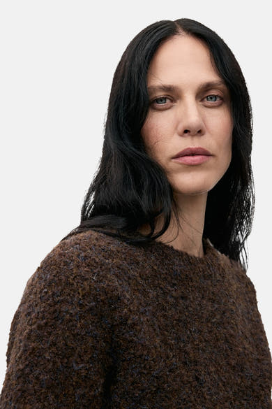 Pull à col rond marron de MANGO, en texture bouclée et douce, porté par une femme aux cheveux noirs.