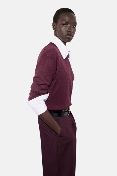 Pull à col rond bordeaux de MANGO, porté avec un chemisier blanc et une ceinture noire.
