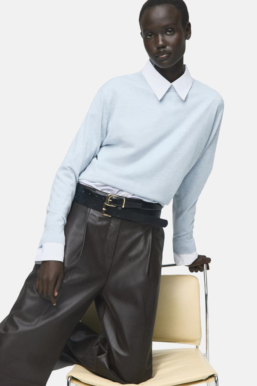 Blauwe trui met ronde hals van MANGO, gedragen met een wit overhemd en een bruine leren broek met riem.