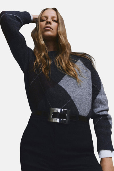 Pull gris à col rond de MANGO, avec motif losanges et ceinture noire à boucle argentée.

