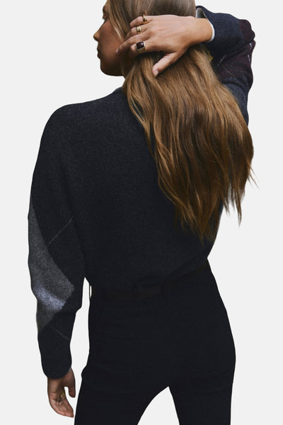 Pull à col rond gris de MANGO, avec motif losanges sur les manches et porté avec un pantalon noir.