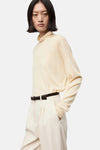 Pull à col roulé écru de MANGO, porté avec une ceinture noire et un pantalon blanc cassé.